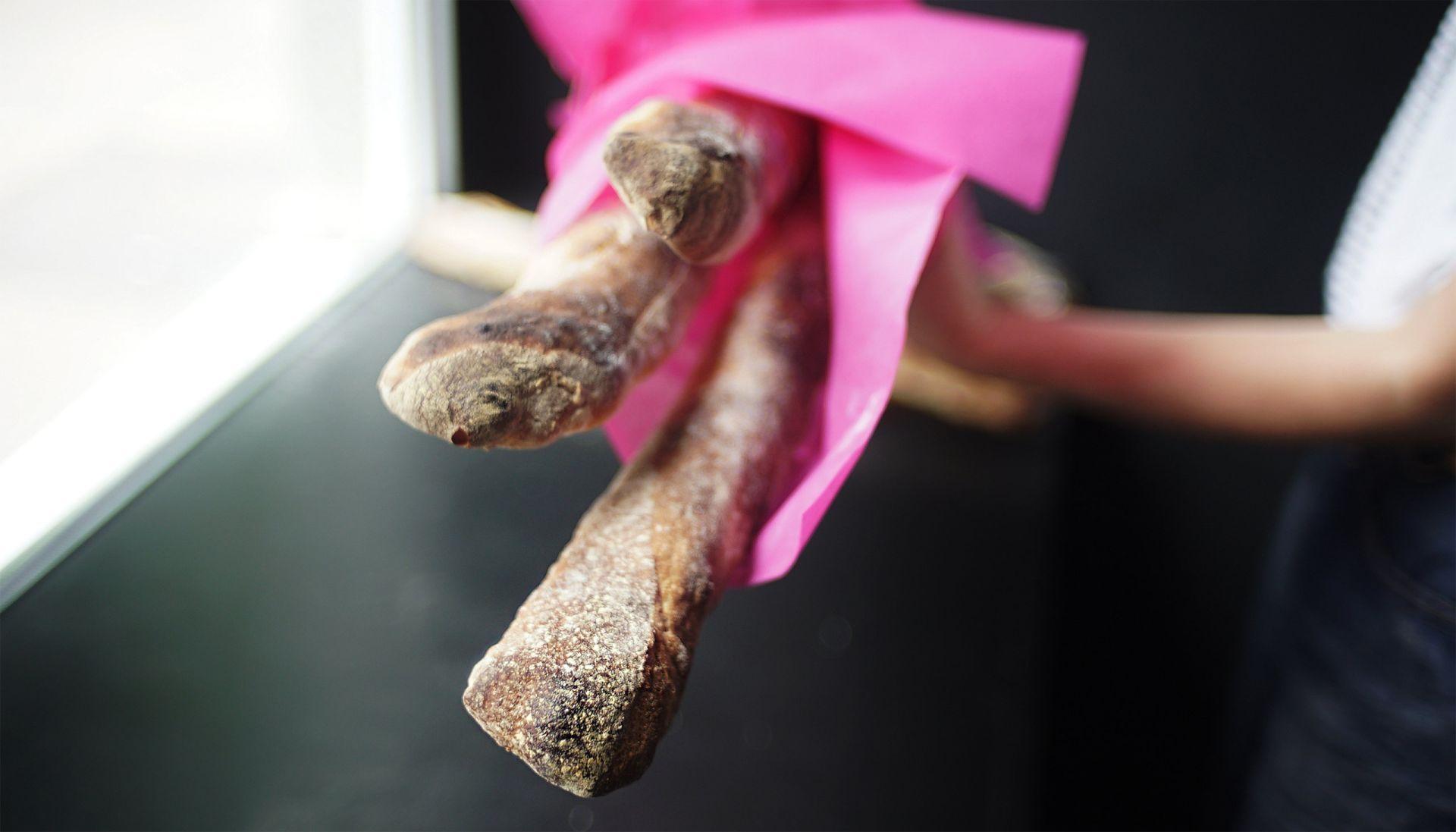 Close-up of baguettes wrapped in pink paper held by a person near a window.