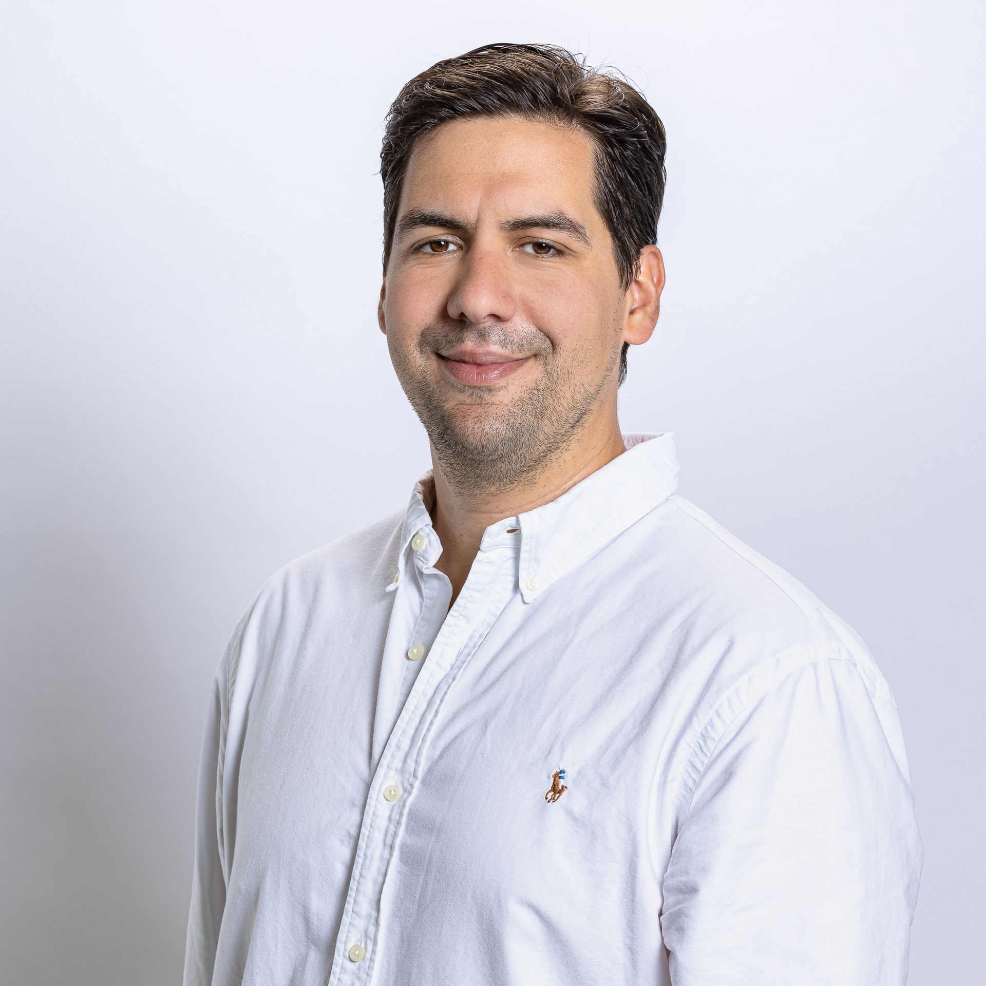 Man in a white button-up shirt smiling against a light background.